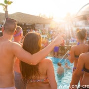 Sexy hot frinds dancing on a beach party event in sunset. Crowd dancing and partying at poolside in background. Summer electronic music festival. Hot summer party vibe.